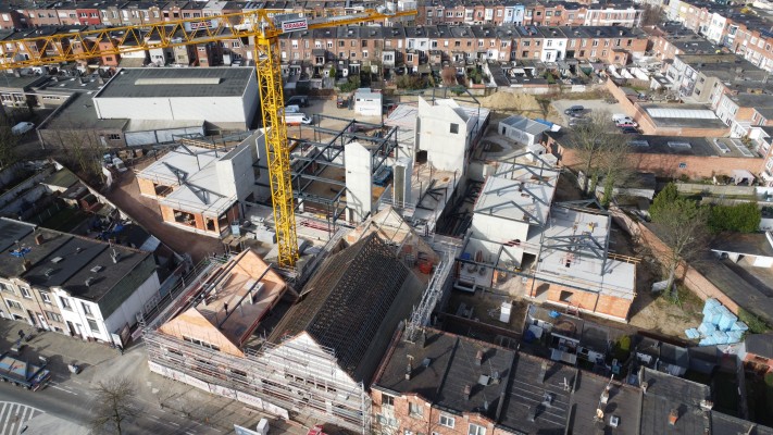 Luchtfoto genomen tijdens de bouw van de school met torenkraan en gebouwen in werf.